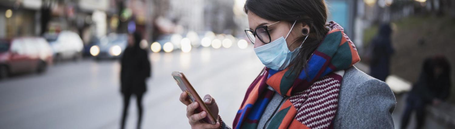 Woman wearing a mask looking at her phone on an empty street.