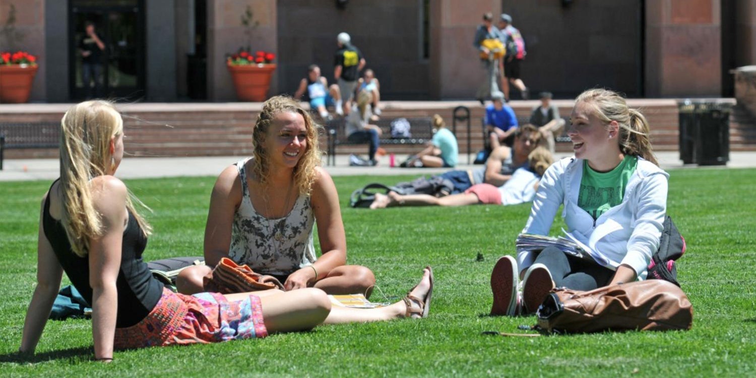 three female students sitting in the grass