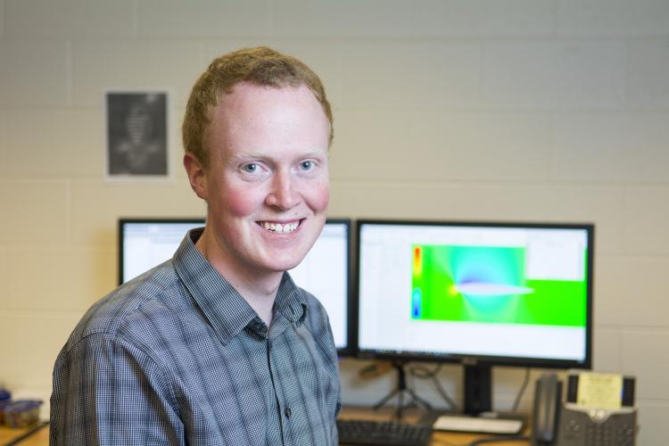 Portrait of CU student Matthew Hurst in front of monitors displaying his computer modeling graphics