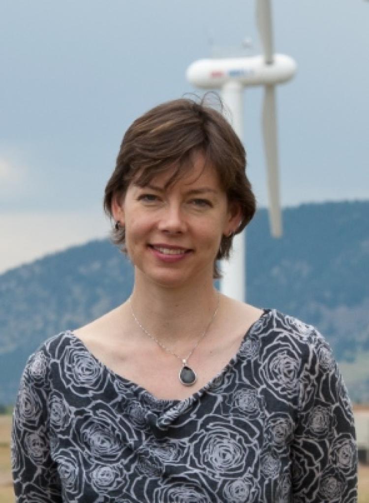 Julie Lundquist portrait with a faded wind turbine behind her and a out of focus hill behind that.