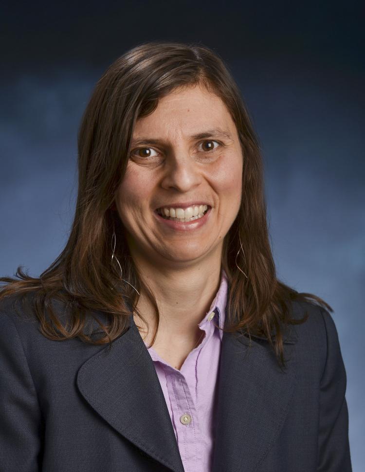 Juliet Gopinath wears a blue blazer in a portrait with a blue background. 