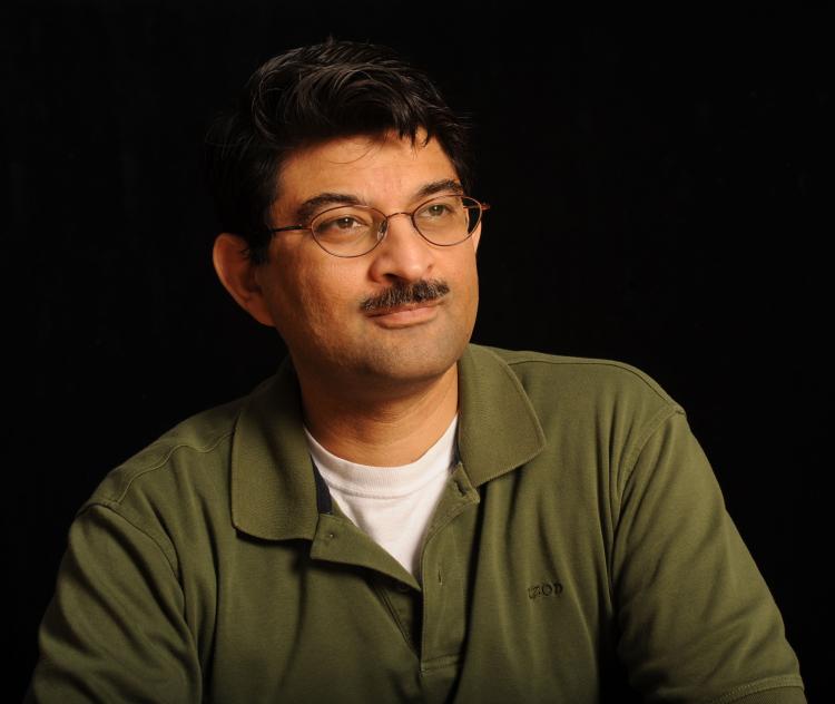 Portrait of Khurram Afridi looking to the right  in a green shirt with a black background.