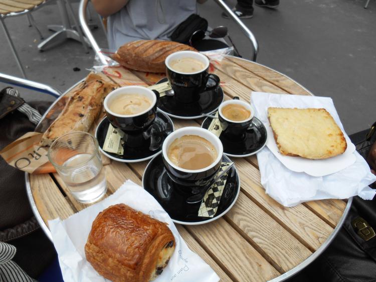 Four cups of coffee and an assortment of pastries are pictured on a cafe table.