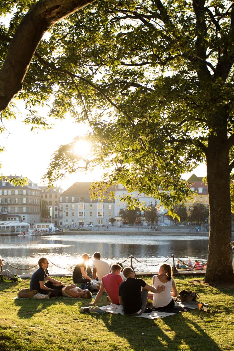Students sit on the banks of the river as the sun sets over Copenhagen, Denmark.