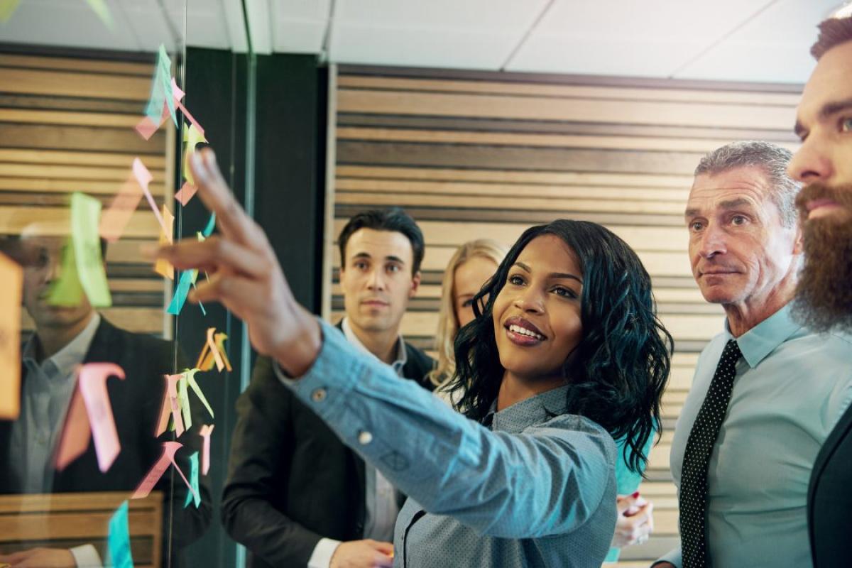 People gathered around a woman putting sticky notes on a board