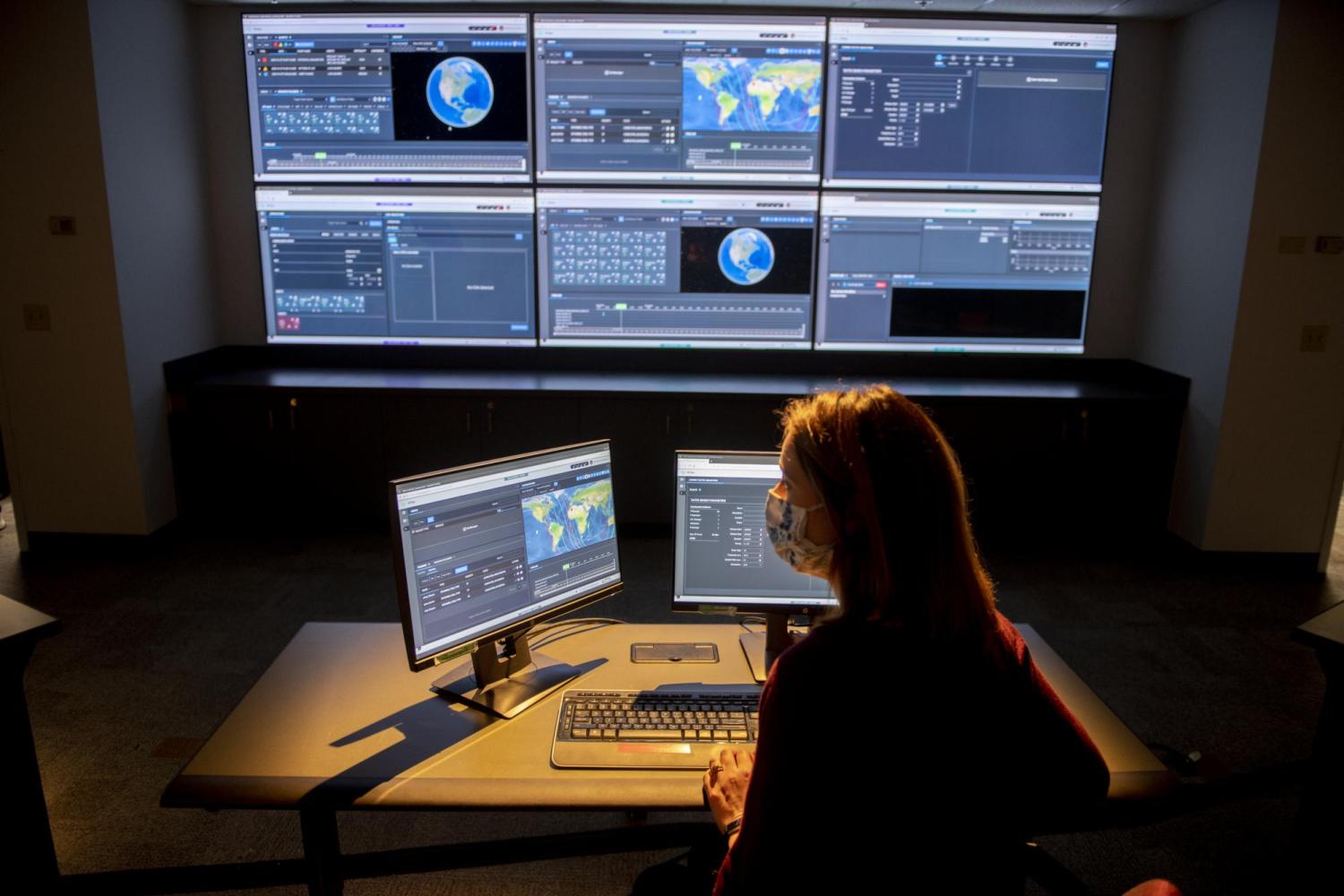 Employee of Raytheon works at a computer in front of large screen.