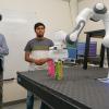 Morteza Lahijanian and graduate student Karan Muvvala watch as a robotic arm completes a task using wooden blocks.