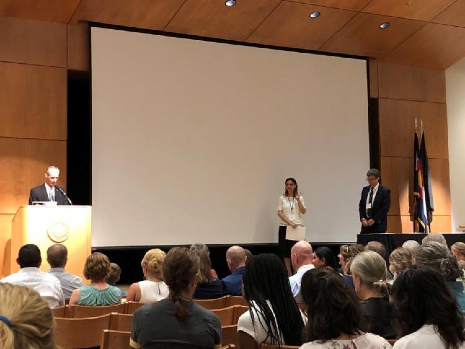 a female instructor and male presenter on the stage in front of audience