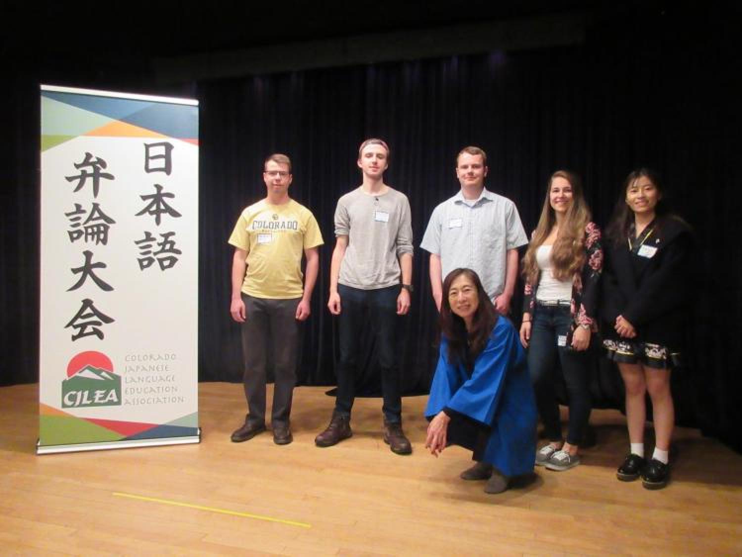 several students and an instructor posing next to the Japanese Speech Contest sign