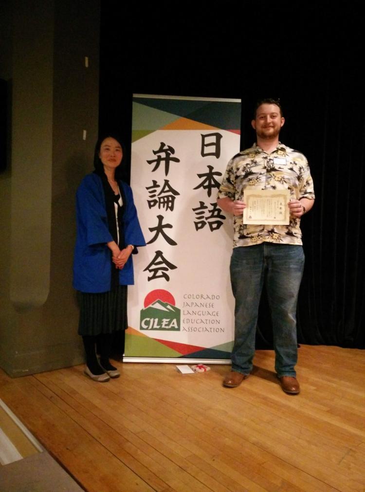 A male student and a female instructor standing next to the Japanese Speech Contest Sign
