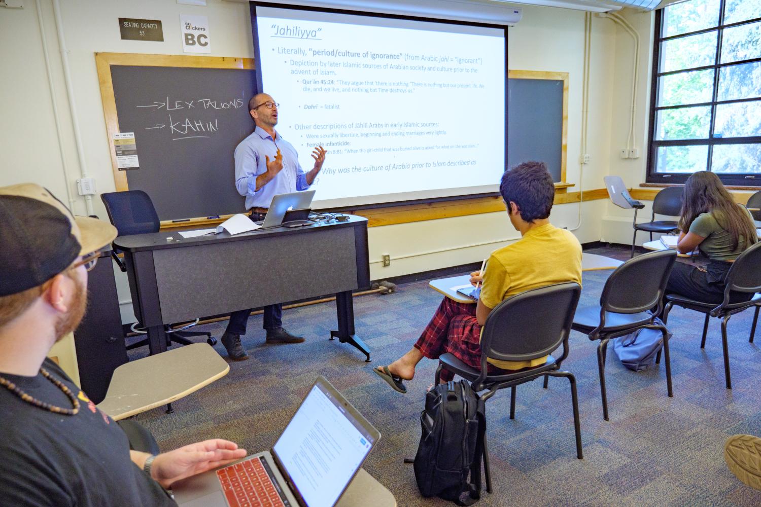 A male professor standing in front of the screen, lecturing