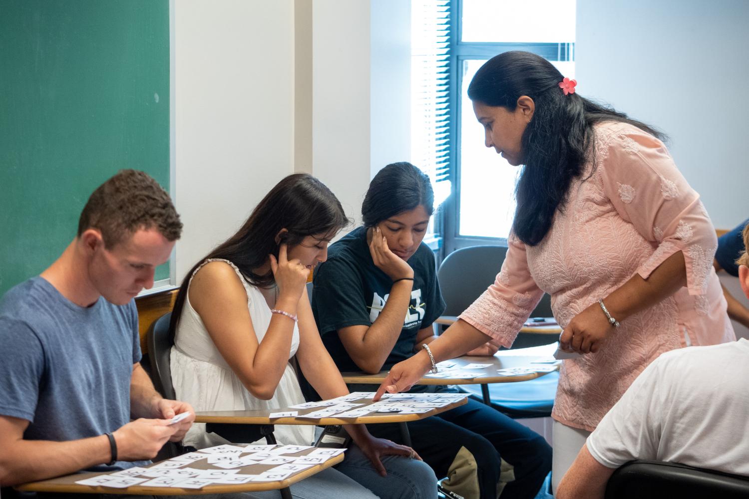 A female professor pointing at document while three students sitting and looking at materials