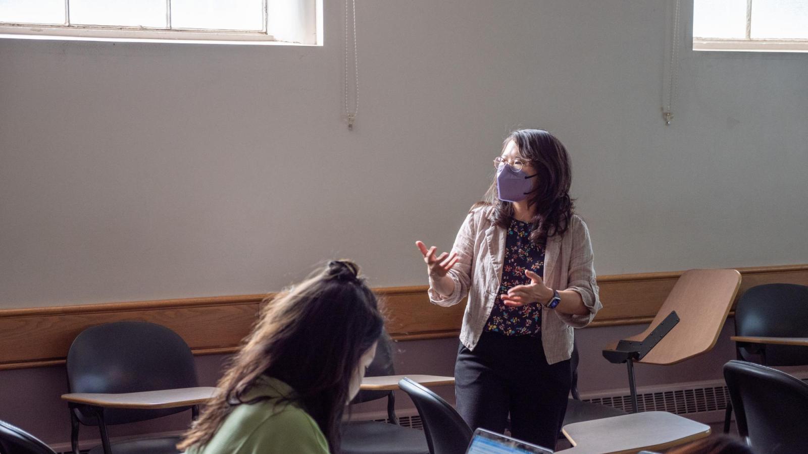 A female instructor standing and talking in the middle of the classroom