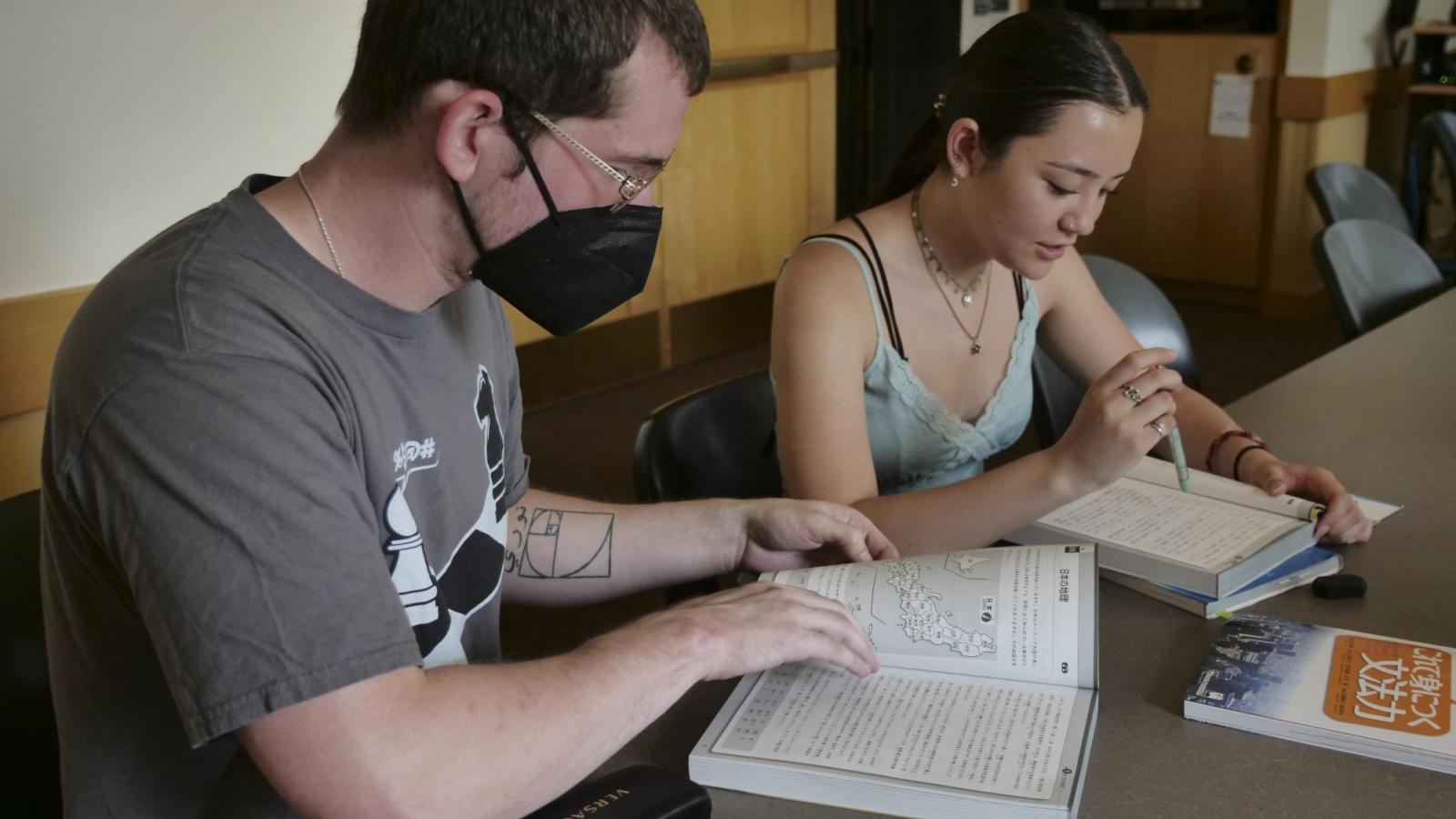 A female student and a male student reading a textbook in Japanese
