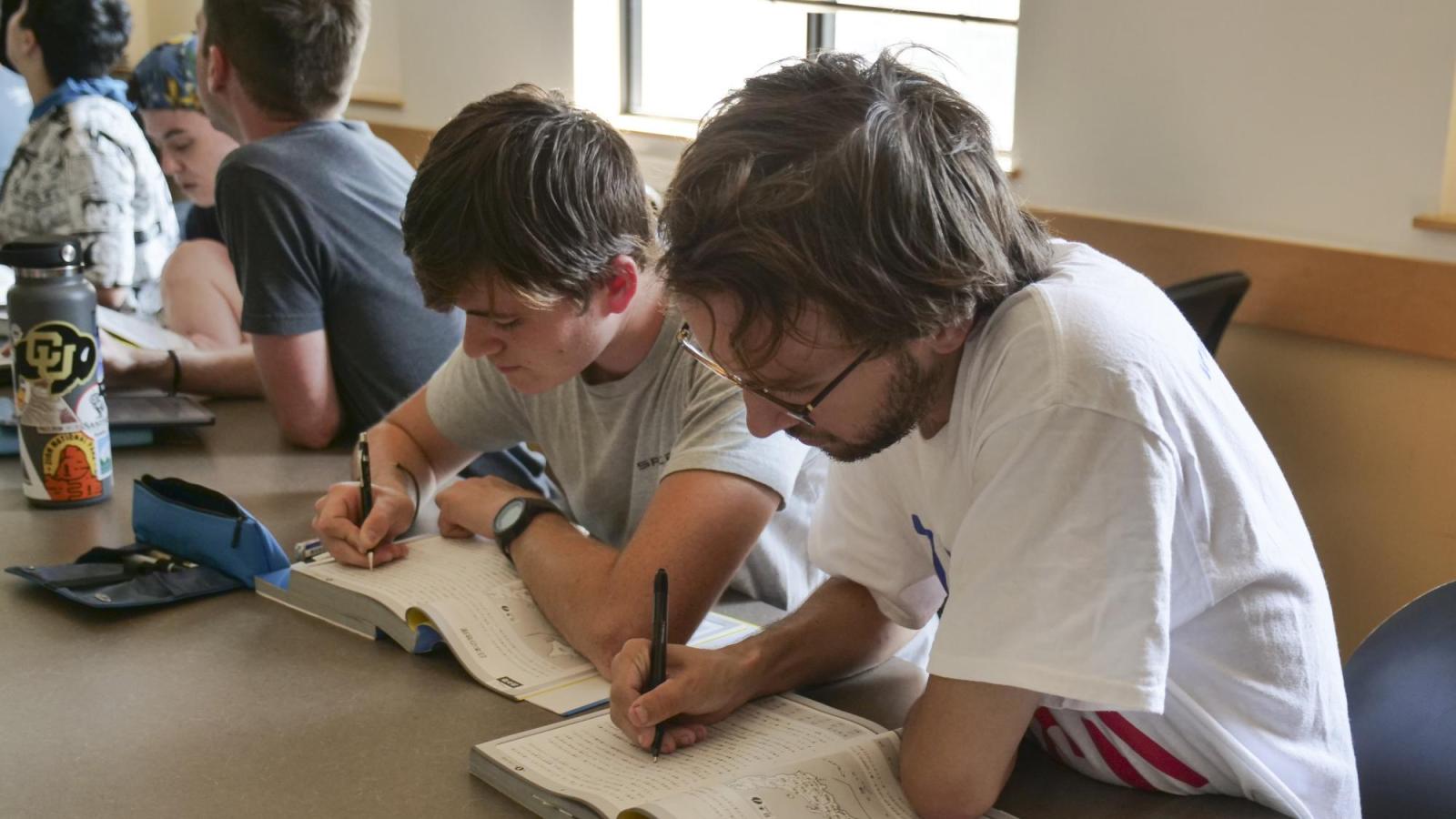 Two male students writing on a notebook