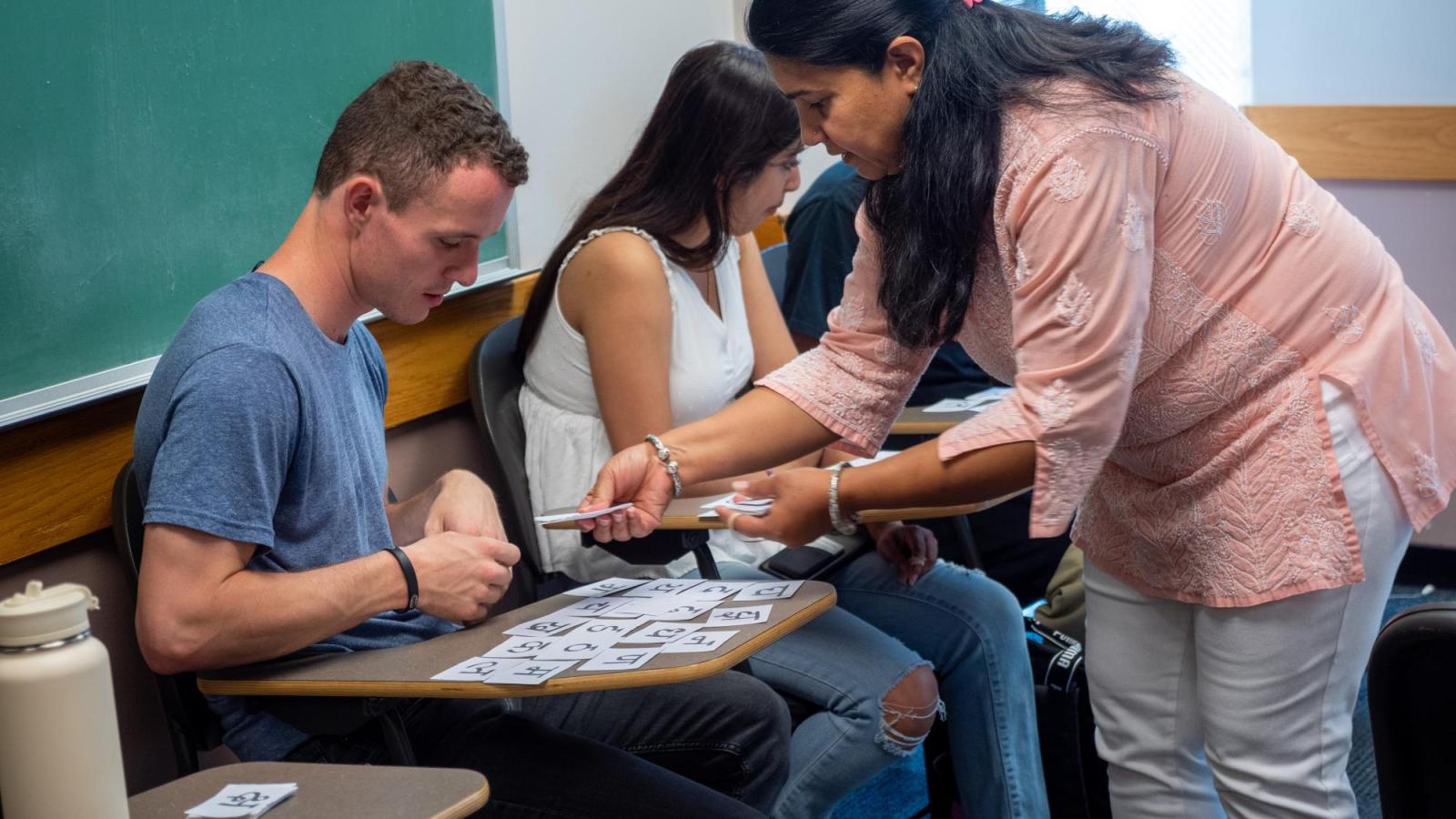 A female instructor handing a Hindi alphabet card to a male student