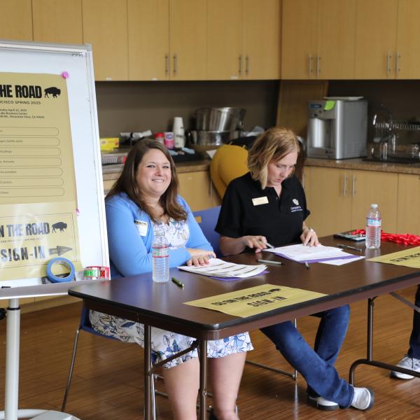 two people sitting at table, one person standing