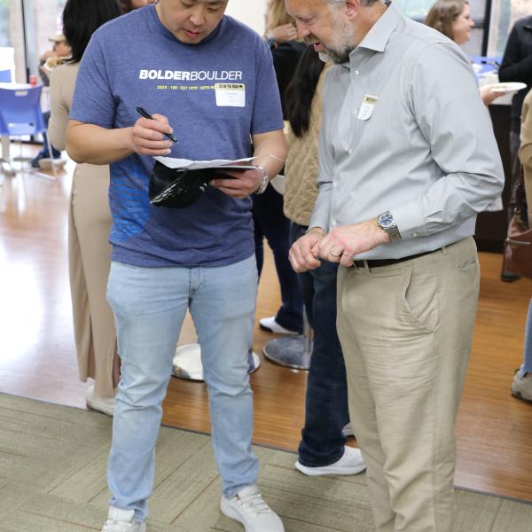 2 people standing and looking at a paper one is holding
