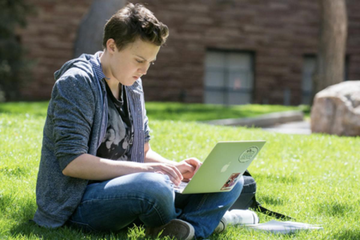 a student on cu boulder campus sits while typing on a laptop