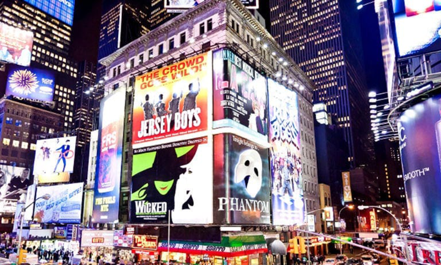 Times Square at night with lots of show billboards and yellow taxis