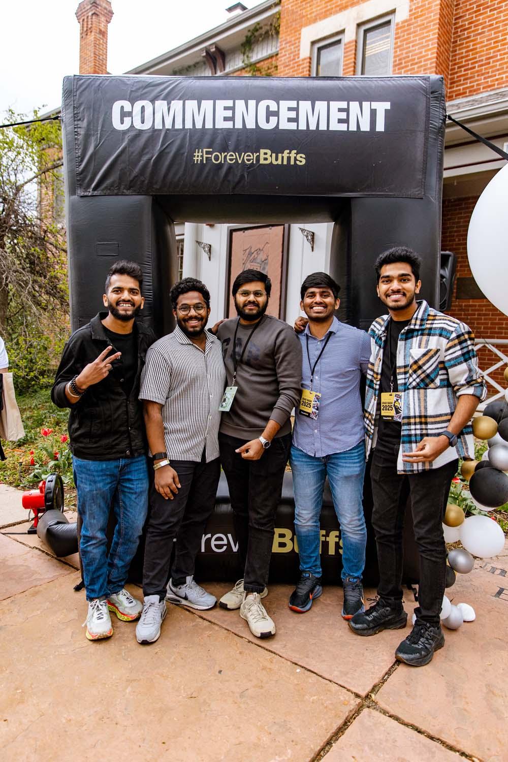A group of CU Boulder graduates pose for the camera in front of a commencement inflatable photo backdrop