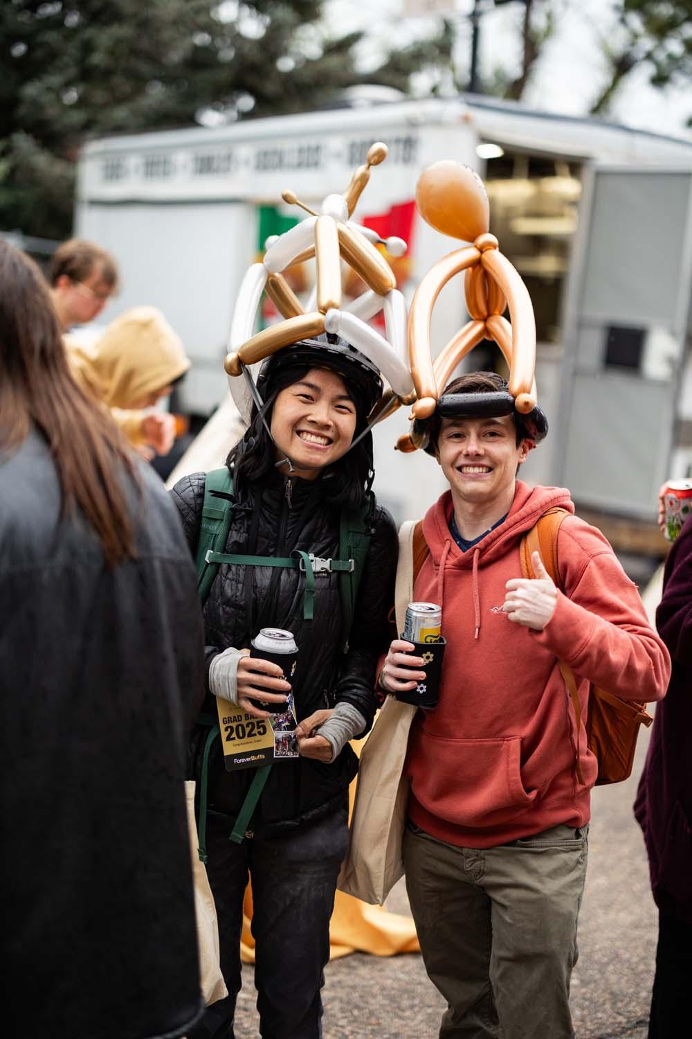 Two CU Boulder graduates pose with balloon art hats on their heads