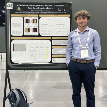 Ethan Coleman standing next to his poster at a conference.