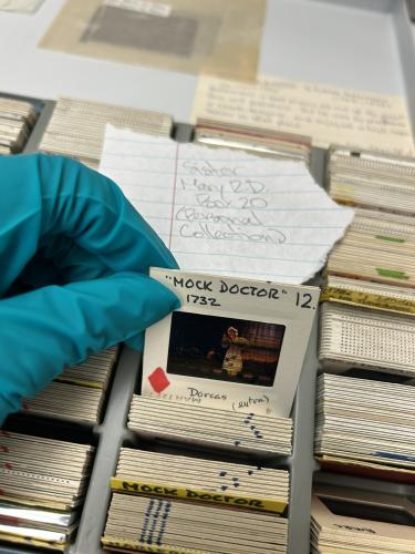 A hand holding a photo slide in front of a box of slides. The slide says "The Mock Doctor"