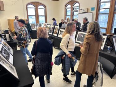 Picture frames set up on long tables and people standing in between the rows, admiring the photos.