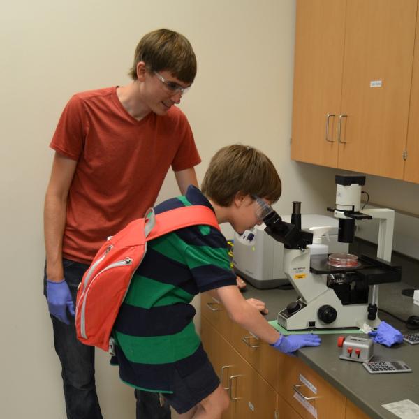 Kyle Kyburz showing a young scientist migrating stem cells at the CU Science Discovery Camp..