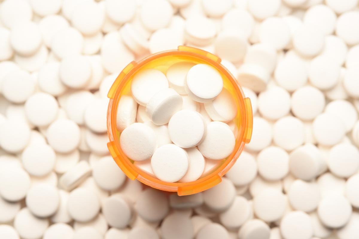 Photo of an open prescription pill bottle surrounded by round white pills.