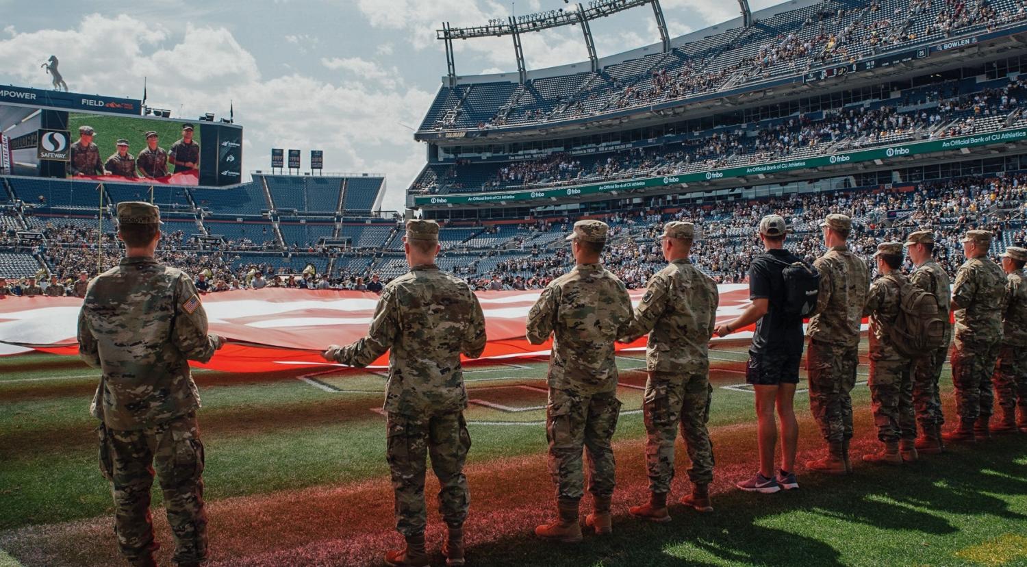 Army ROTC Cadets holding the U.S. flag and watching themselves on the big jumbotron screen. Photo courtesy of Cadet Arianna Decker.