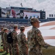 Army ROTC Cadets holding the U.S. flag and watching themselves on the big jumbotron screen. Photo courtesy of Cadet Arianna Decker.