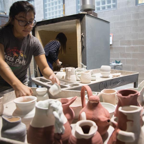 Student with clay sculptures loading into the kiln