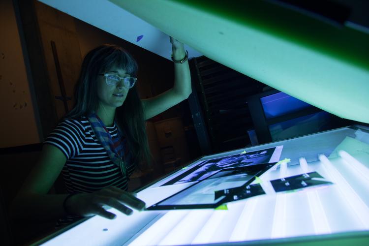 Student reviewing negatives at the light box in the darkroom studio