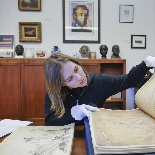 A student browses a massive historical text while wearing white gloves.