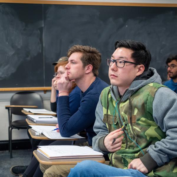 Students watch a lecture in a blackboard-lined classroom.