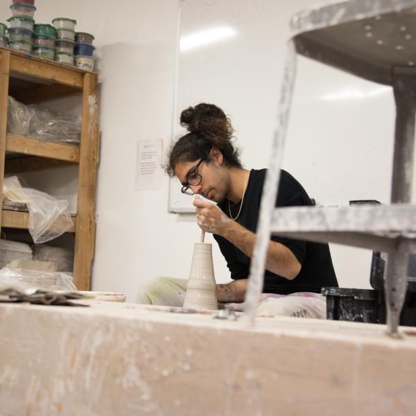 a student molds a clay pot on a potter's wheel.