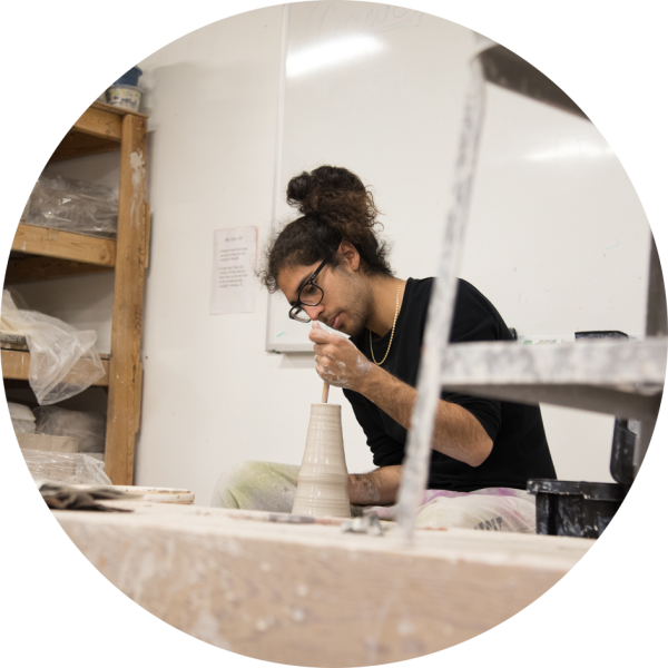 A student throws a clay pot on a potter's wheel.