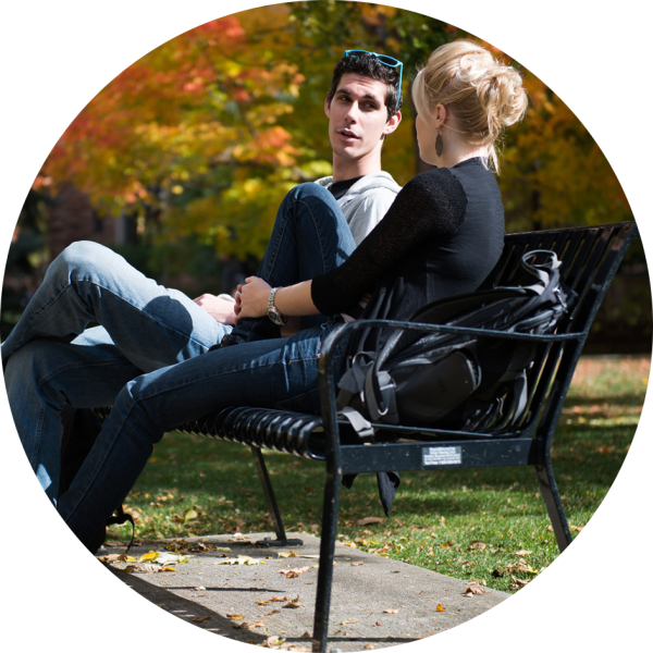 A student sits on a bench and discusses a concept with a faculty member