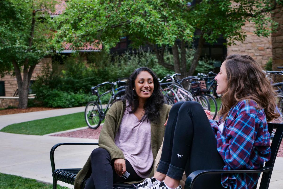 Two students sit on a bench and have a friendly conversation.