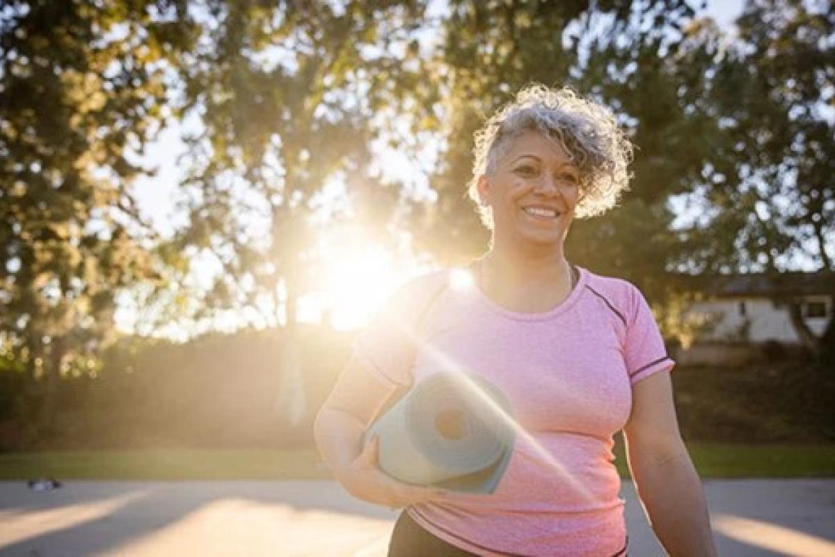 smiling woman holding a rolled-up yoga mat