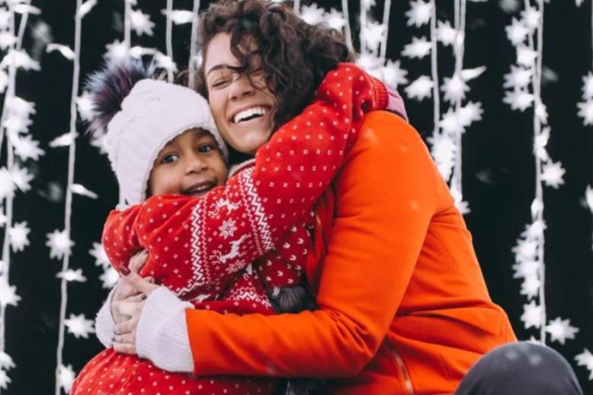 kid and woman hugging in front of a string of snow flake lights