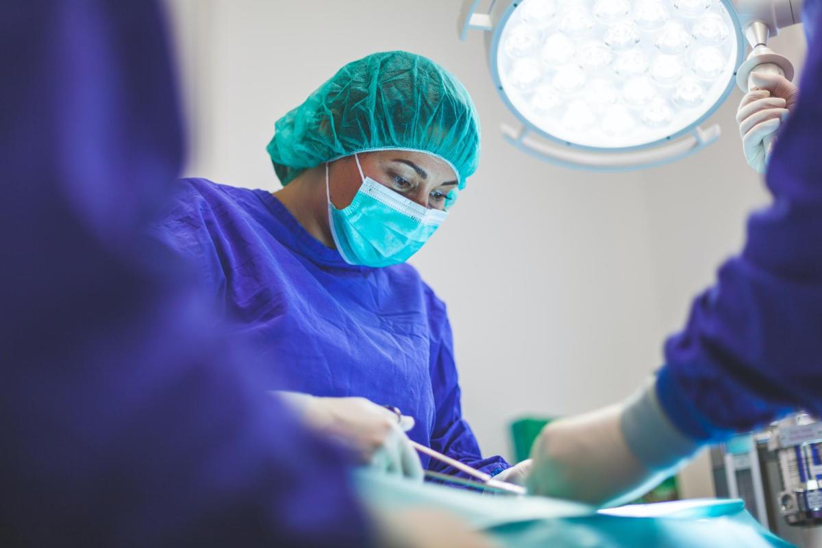 A surgeon begins a stitch while in a large surgery room.