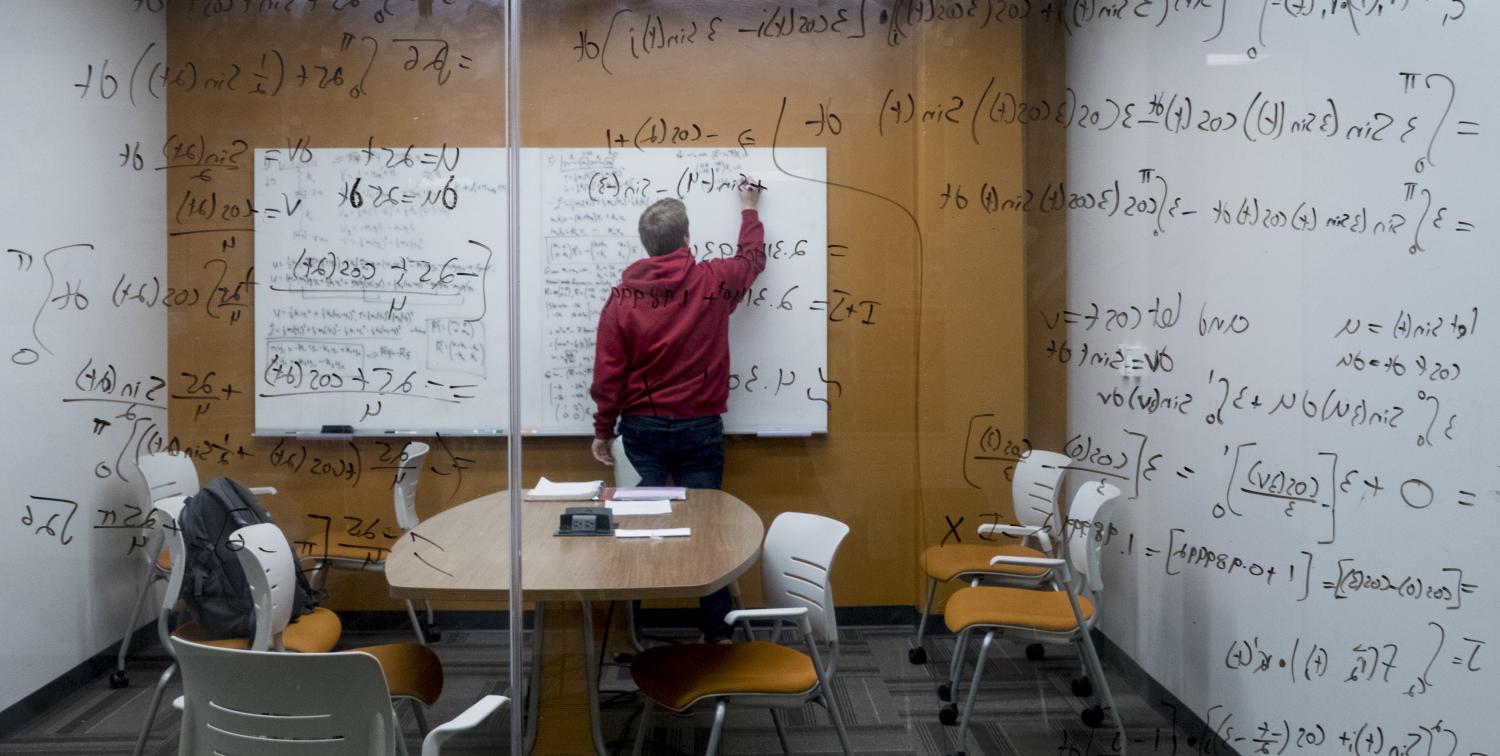 A student writes on a window while trying to solve an algorithm.