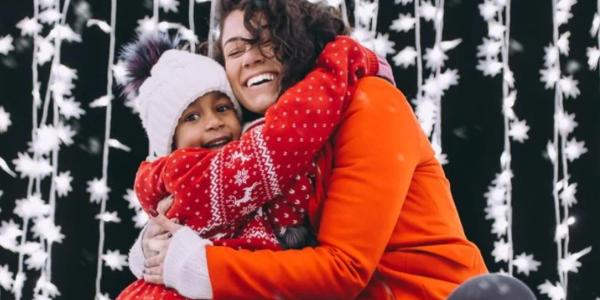 kid and woman hugging in front of a string of snow flake lights