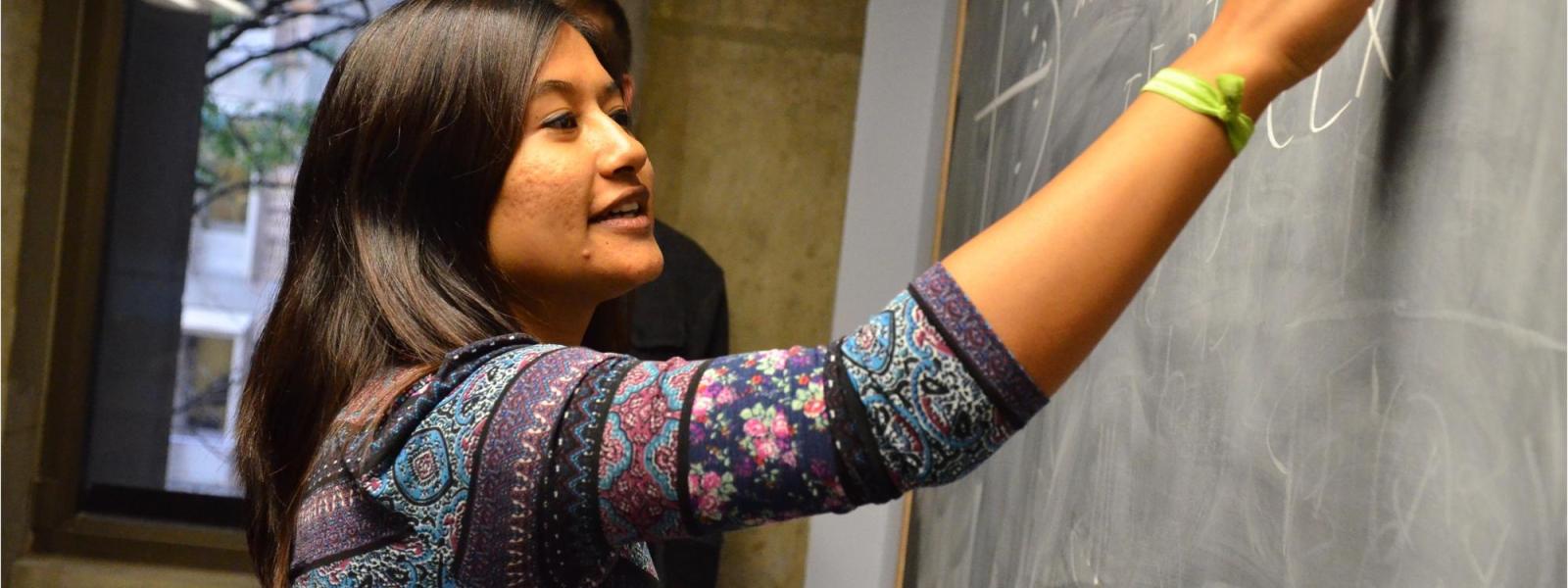 student solves a math problem on a chalk board