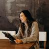 A woman holding a tablet, laughs at someone or something she sees to her right.