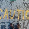 Feet stand before "Caution" written on chalk on a street.