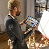 a man looks at a tablet in front of a blank canvas.